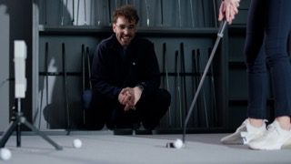 Image of a man kneeling on the ground in an indoor putter fitting studio analyzing a customer's putting stroke.