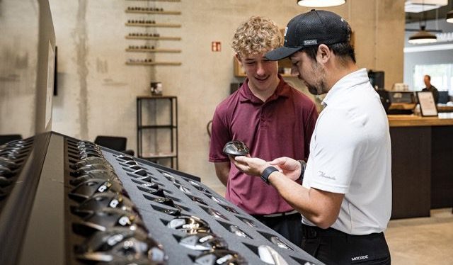 Image of a young golf club fitter showing a hybrid club to a young customer.